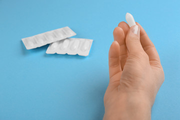 Woman holding suppository on light blue background, closeup. Hemorrhoid treatment
