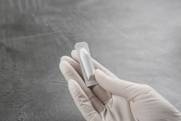 Woman holding suppository at grey table, closeup. Hemorrhoid treatment