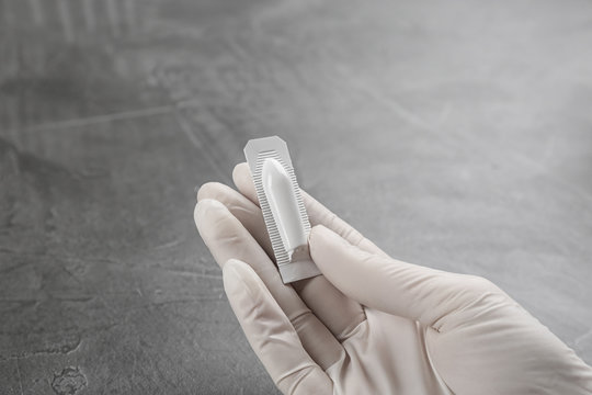Woman holding suppository at grey table, closeup. Hemorrhoid treatment