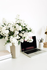 Laptop with mockup blank copy space screen on table. Office desk workspace with flowers bouquet, table lamp. Minimal freelance co-working concept.