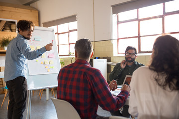 Creative team discussing ideas for startup project, speaker at board pointing at audience. Business colleagues in casual working together in contemporary office space. Brainstorming concept