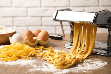 Pasta maker machine with dough and products on wooden table