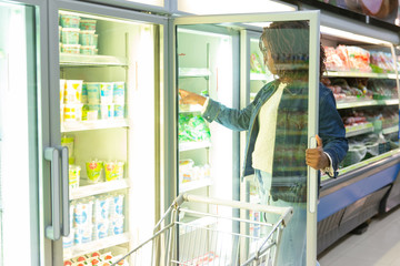 Fototapeta na wymiar African American female customer taking package from fridge shelf in grocery store, choosing fresh food. Buyer shopping in supermarket. Grocery shopping concept