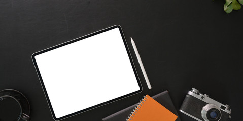 Top view of dark modern workplace with blank screen digital tablet with office supplies on black table