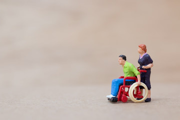 Miniature people : Disabled man sitting in wheelchair  on on wooden background , Accident concept