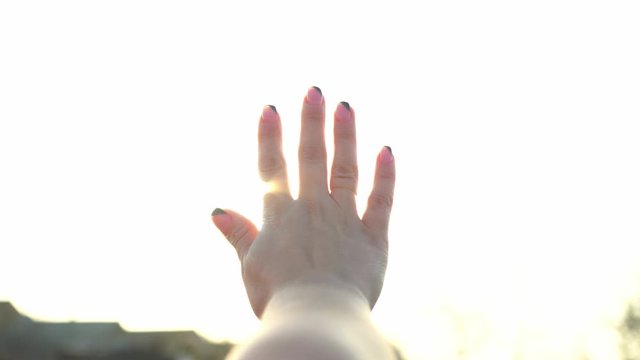 A woman looks at the bright sun through her hand. The magical rays of the sun shine through your fingers. Fantastic bright light. Flash. A woman basking in the sun. Carelessness. Happiness. Tourism.
