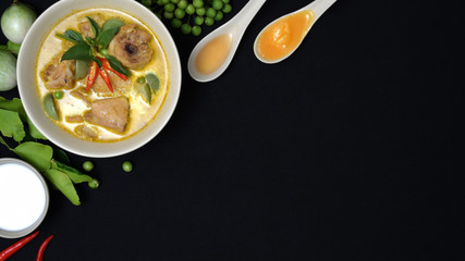 Top view of chicken green curry and ingredients on black desk background, Thai cuisine concept