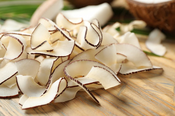 Pile of tasty coconut chips on wooden board, closeup