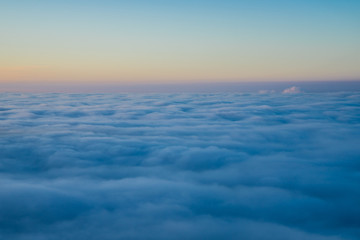 Endless aerial view above fluffy clouds at sunset from the top of a mountain in winter, a beautiful nature landscape