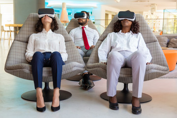 Group of concentrated coworkers in VR headsets. Front view of multiethnic businesswomen and...