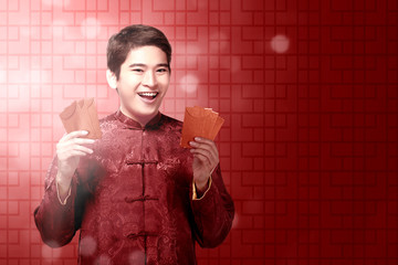 An Asian Chinese man in a cheongsam dress holding red envelopes