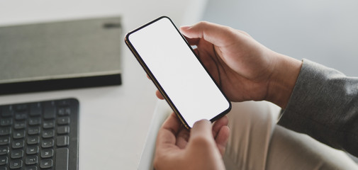 Cropped shot of young businessman working on his project while using blank screen smartphone in modern office