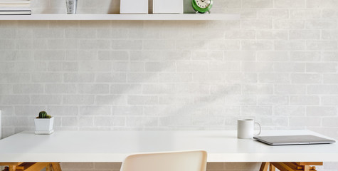 Cropped shot of comfortable workplace with office sullies on wooden table and white brick wall