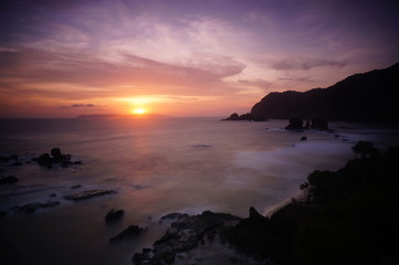 sunset and sunrise are the natural beauty at the end of the night and at dusk giving the perfect color to the sky so the clouds look beautiful to be seen with the beach set against a mountain.