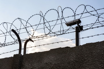 Security camera behind barbed wire fence on the wall, prison, security, crime or illegal...