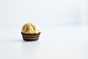 one candy in gold foil on a light background