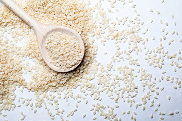 Organic natural sesame seeds and a wooden spoon on a white background