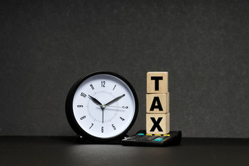 Tax Concept with tax word on wooden block, clock and calculator over black background