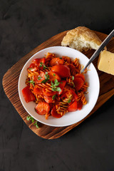 Plate of italian pasta with tomato sauce, roasted red peppers, carrots and basil on wooden serving board. Tasty homemade food on black background. Vertical orientation, top view
