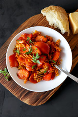 Plate of italian pasta with tomato sauce, roasted red peppers, carrots and basil on wooden serving board. Tasty homemade food on black background. Vertical orientation, top view
