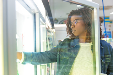 Young female customer taking food from fridge shelf in grocery store. Buyer shopping in supermarket. Buying fresh product concept