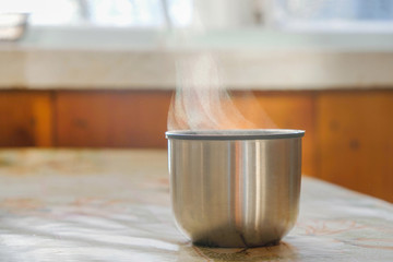 Metal thermos cup with tea on the table on a sunny cold day in Ukraine. The hot liquid evaporates.