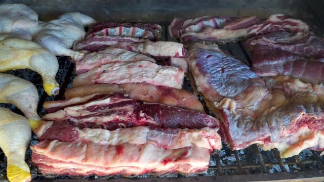 Raw pieces of beef and chicken starting to roast in Argentinian asado