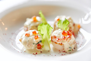 fried scallops on a plate, sprinkled with caviar sauce, garnished with salad, seafood