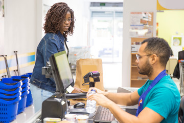 Side view of male cashier scanning goods at checkout. Young woman with buying groceries in...