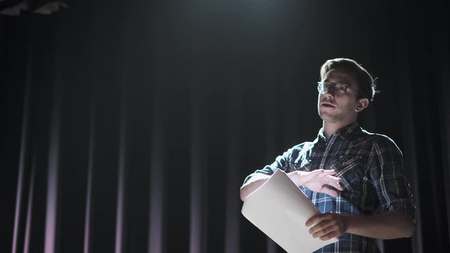 Medium shot of actors and actresses rehearsing a scene in a theater. Medium shot of an actor performing a monologue in a theater while holding his script