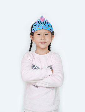 Portrait of confident little Asian child girl with wearing a crown toys and cross one arm isolated over white background.