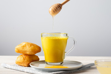 Golden milk with turmeric and honey, a traditional Indian drink on a white wooden background