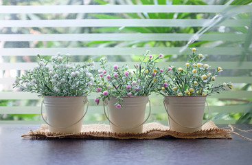 Plastic decoration flower in small pot on wooden table.