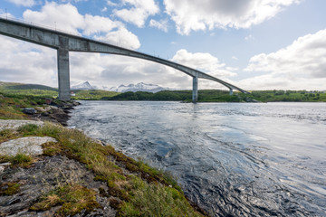 Bridge over Saltstraumen river in Bodo in Northern Norway. Snow covered mountains in the background and blye cloudy sky. Traveling and holiday concept.