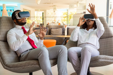 Coworkers in VR headsets moving hands. Focused young African American businessman and businesswoman...