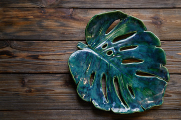 beautiful green large ceramic plate in the shape of a monstera leaf on wooden background