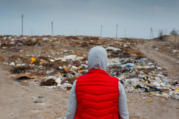 Back view of human in red jacket, looking on a big garbage field.