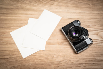 Old retro camera and several empty white photo frames on a light wooden background. Top view in perspective. Free space for text and your photos.