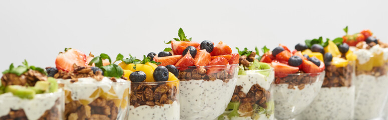 selective focus of delicious granola in glasses with fruits and berries isolated on white, panoramic shot