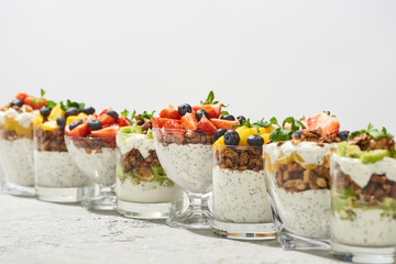 selective focus of delicious granola in glasses with fruits and berries on grey concrete surface isolated on white