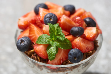 close up view of delicious granola with berries and mint on grey concrete surface