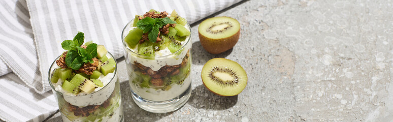 fresh granola with kiwi and yogurt on grey concrete surface with striped napkin, panoramic shot