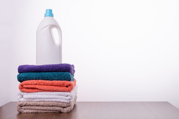 Obraz na płótnie Canvas Folded blue, green, purple, pink, white and beige terry towels and liquid laundry detergent, air conditioning lie on a wooden table on a white background. With copy space.