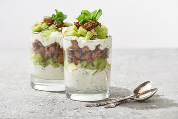 selective focus of fresh granola with kiwi and yogurt near spoons on concrete surface isolated on grey