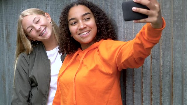 Slow motion video clip of pretty blonde girl and mixed race teenager young women taking selfies on their smart phones for social media