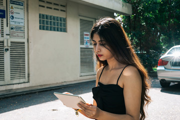 Obraz premium One long hair Indian girl holding and using mobile touch screen device tablet at outdoor park