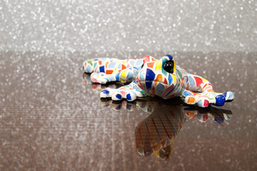 colorful designer lizard on a glass table. Reflex textured glass table. Colourful ceramic model salamander.