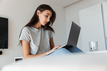 Image of brunette young woman using silver laptop computer at home
