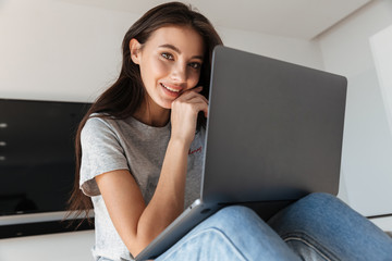 Image of brunette young woman using silver laptop computer at home