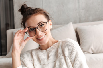 Image of woman in eyeglasses smiling while resting on sofa at home